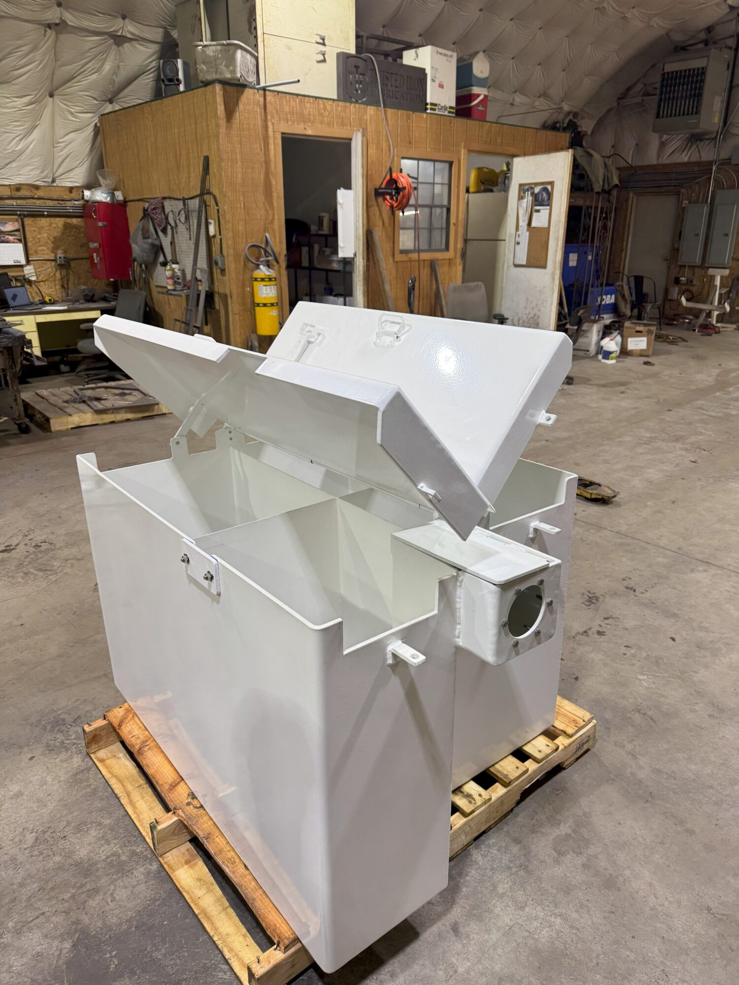 Large white industrial machine with open panels, placed on a wooden pallet in a workshop.