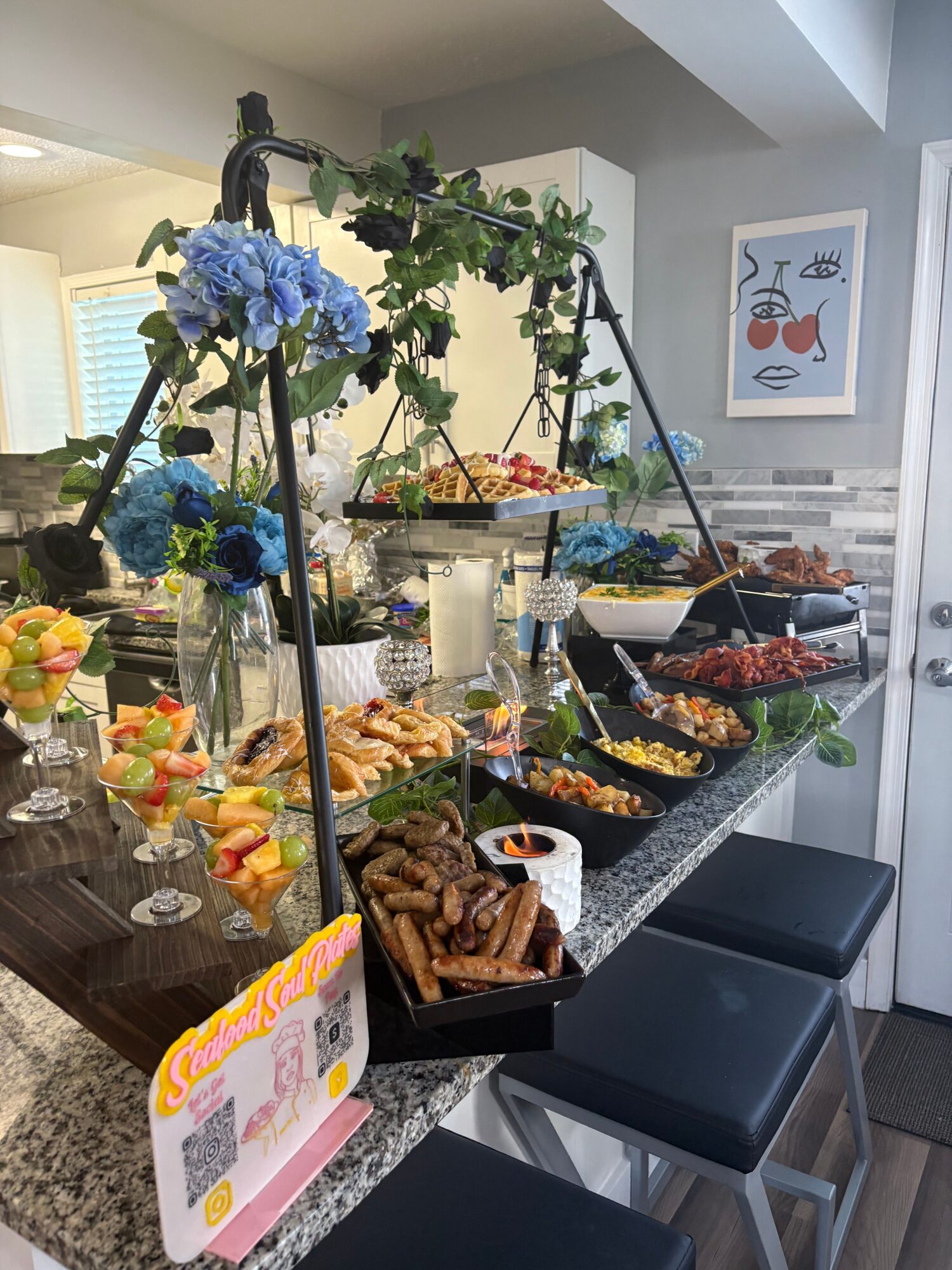 Table with snacks, flowers, and a pink card, in a room with chairs and a window. Flowers are blue and green.