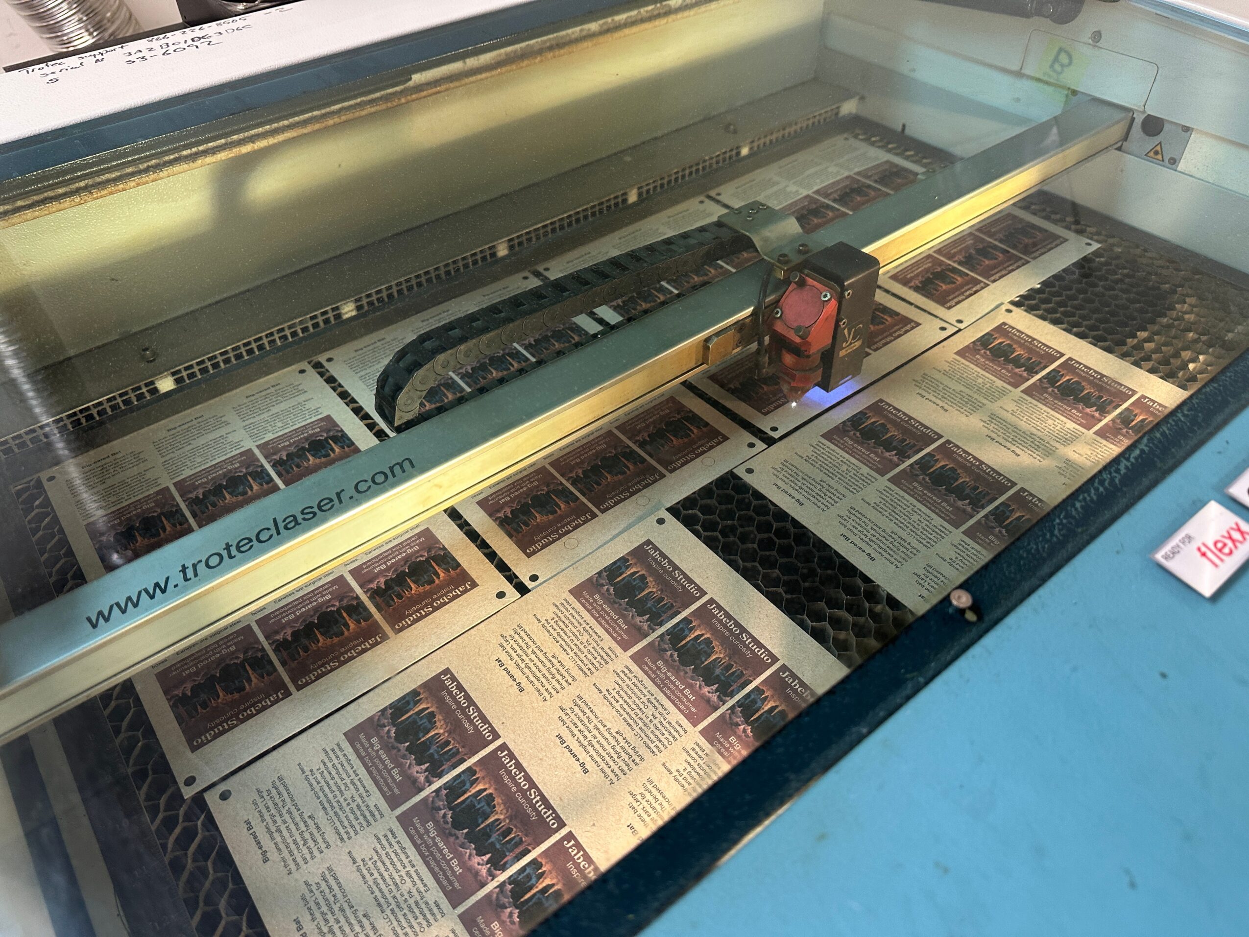 A machine with a glass cover displays printed materials inside, with a blue surface below and a white wall behind.