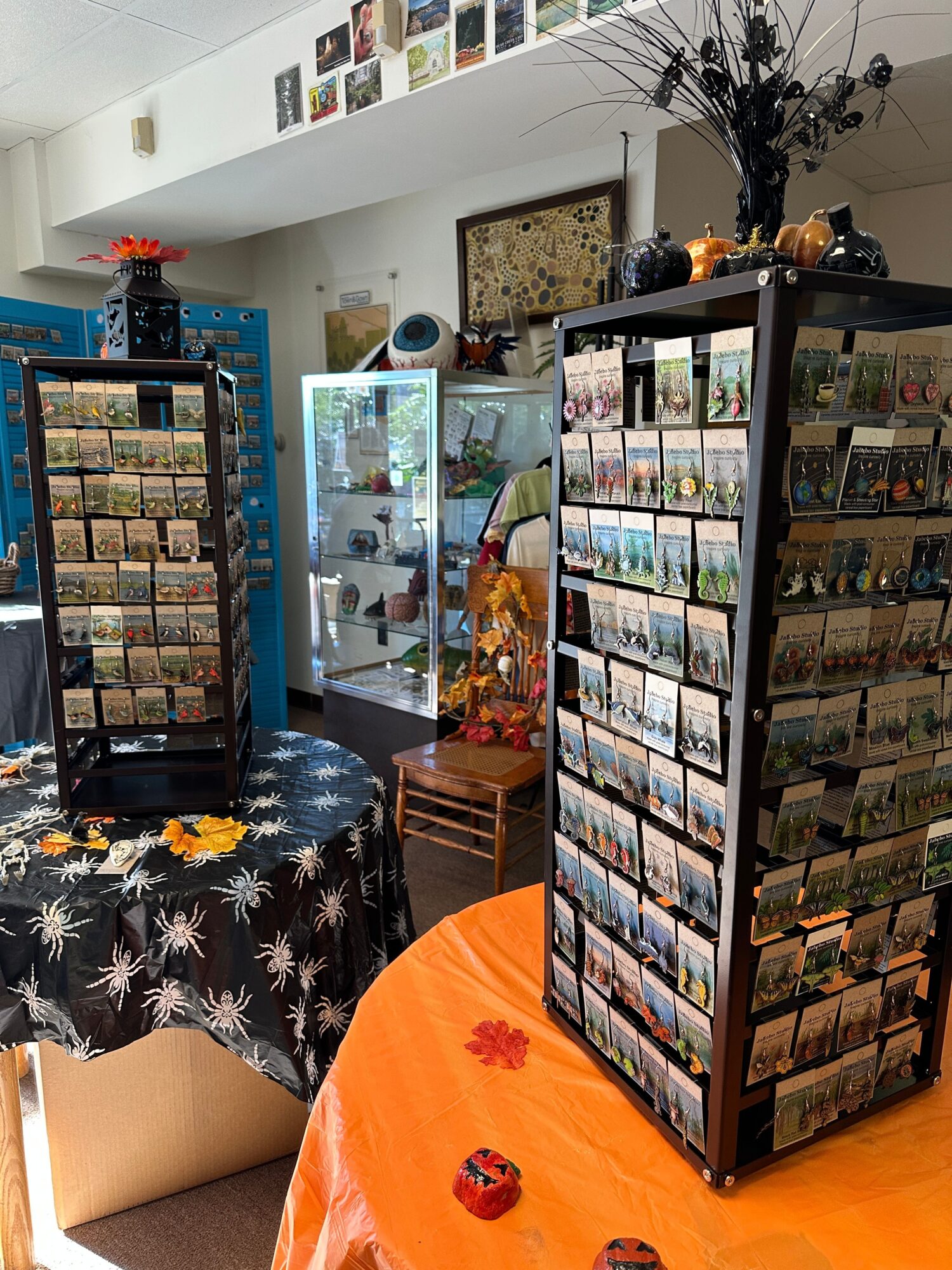 Display case with collectibles, a blue refrigerator, and a table with an orange tablecloth, flowers, and a black and white patterned cloth.