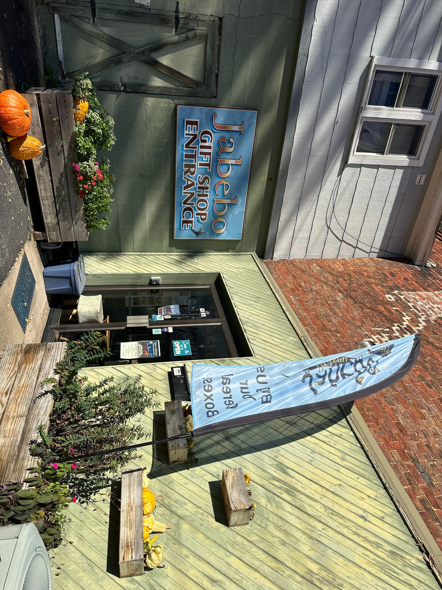 Store entrance with a sign reading 'Jabeho Gift Shop Entrance,' a flag, and flower boxes outside.