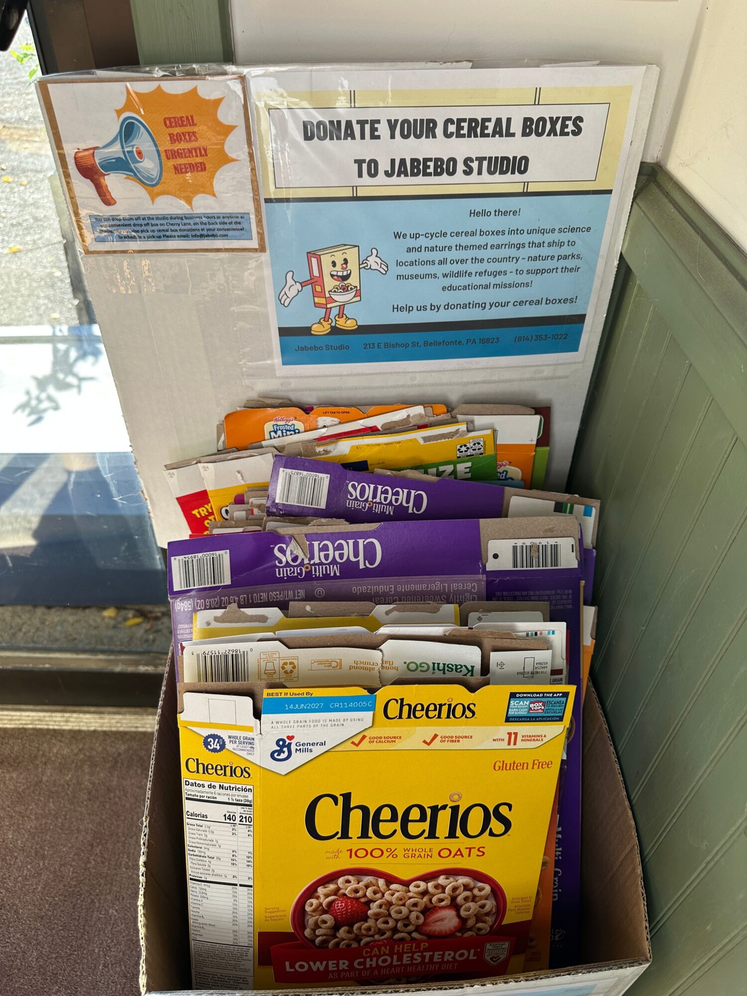 Open cereal box with various cereal boxes inside, including Cheerios and Cherrios, on a table.