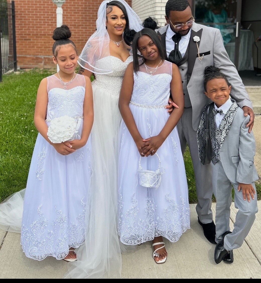 Group of five people, including a bride in a white wedding dress and veil, and four children in formal attire, standing outdoors.