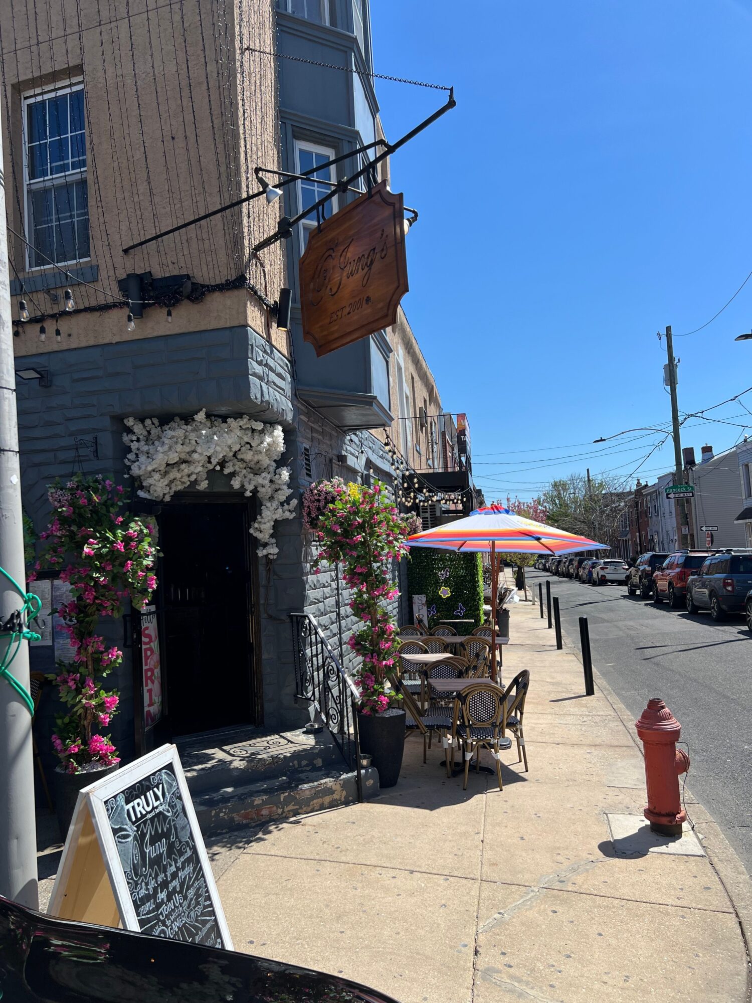 Street scene with storefronts, flowers, sidewalk, and a clear blue sky.