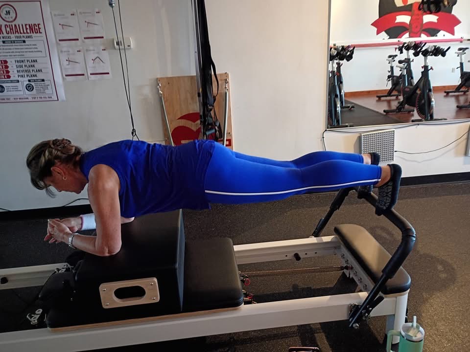Woman in blue workout clothes performs a plank exercise on a fitness machine in a gym.