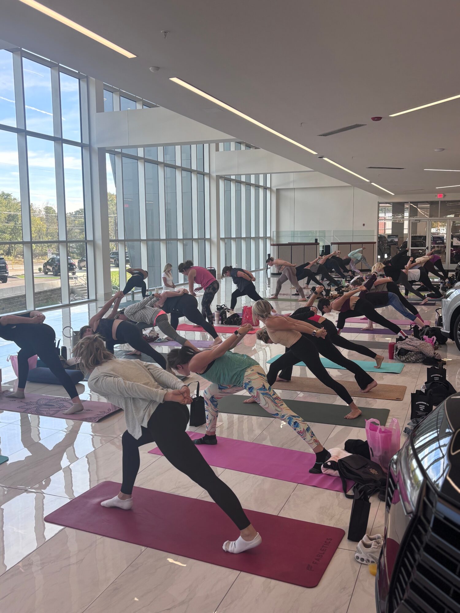 Group of people participating in a yoga class in a bright, spacious room with large windows and natural light.