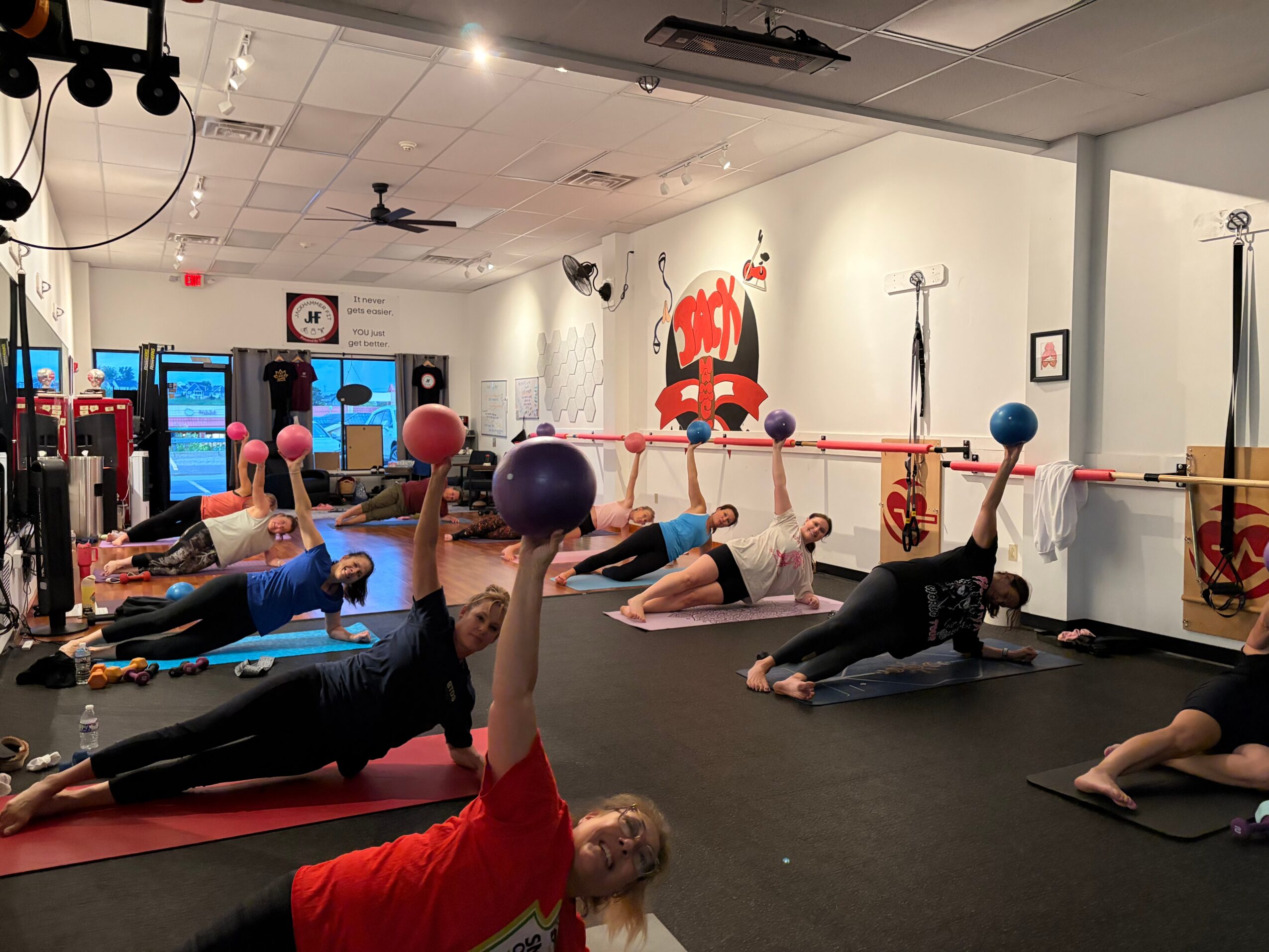 People exercising with balls on mats in a fitness studio with wall art and mirrors.