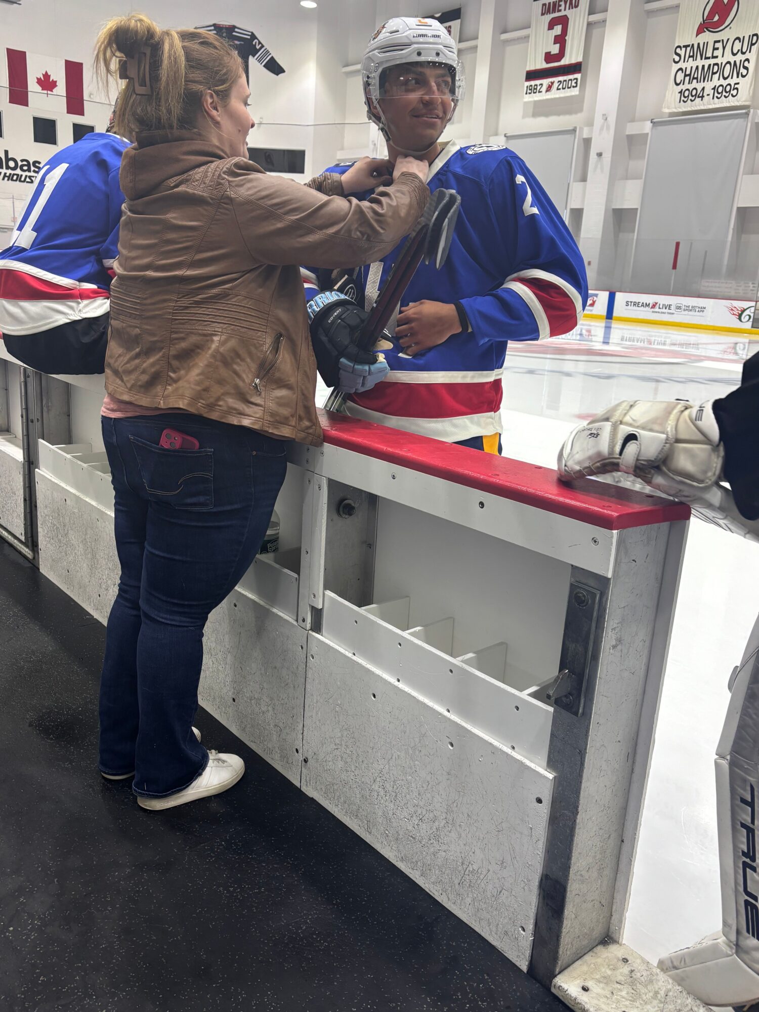 Person in brown jacket at ice skating rink counter, with a person in blue and red jacket nearby, in an indoor setting.