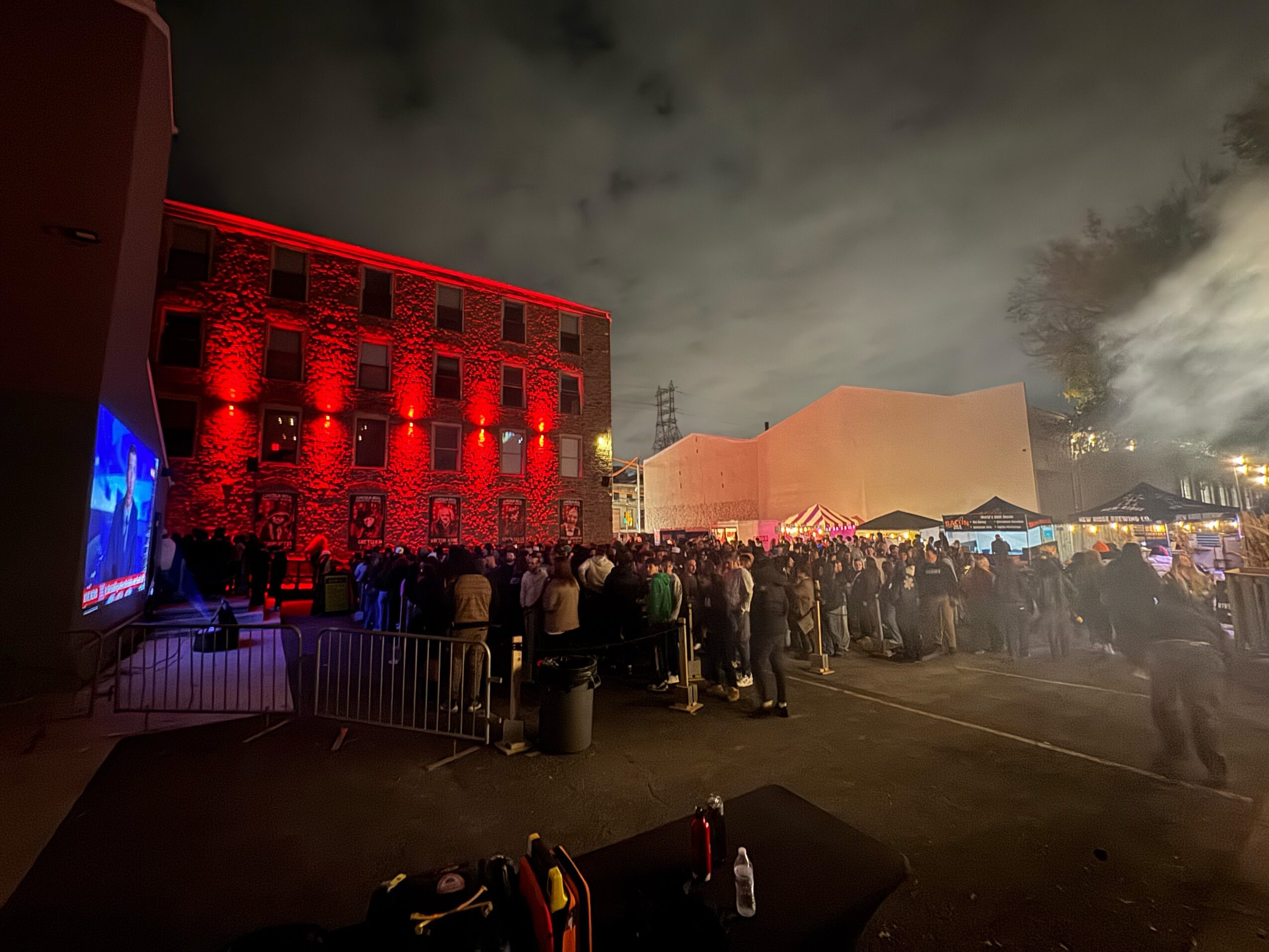 Crowd gathered outside at night with illuminated buildings and smoke in the sky.