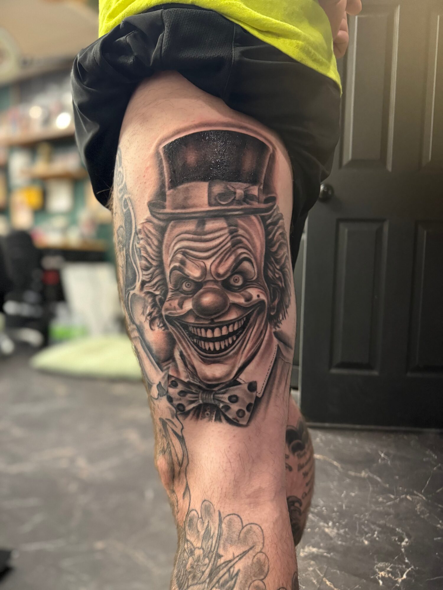 Tattoo of a clown with a big smile, wearing a top hat, on a person's thigh.