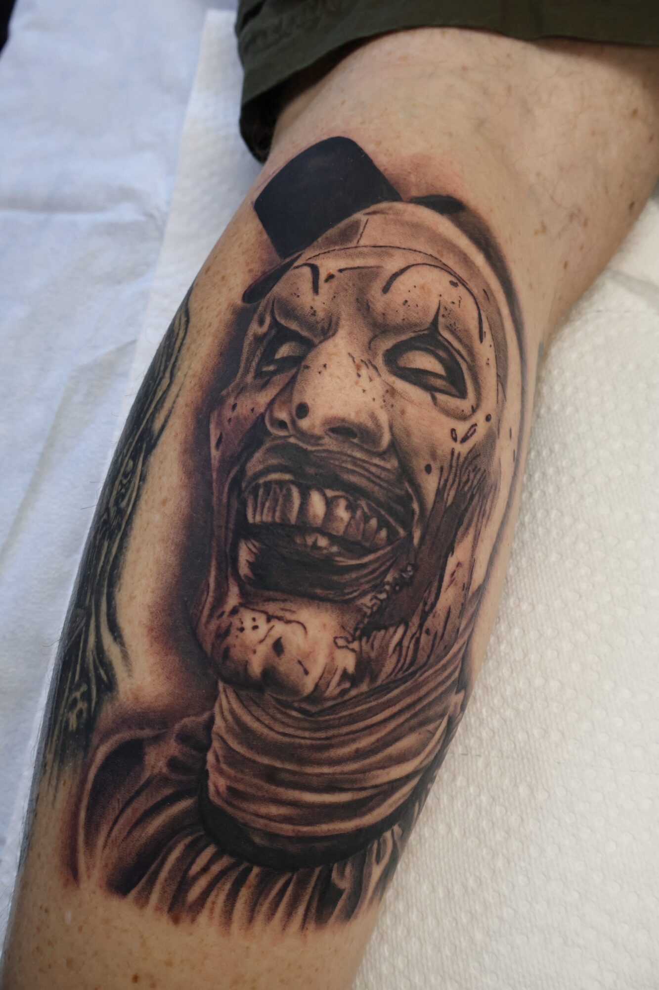Tattoo of a screaming clown face with exaggerated features on a person's arm.