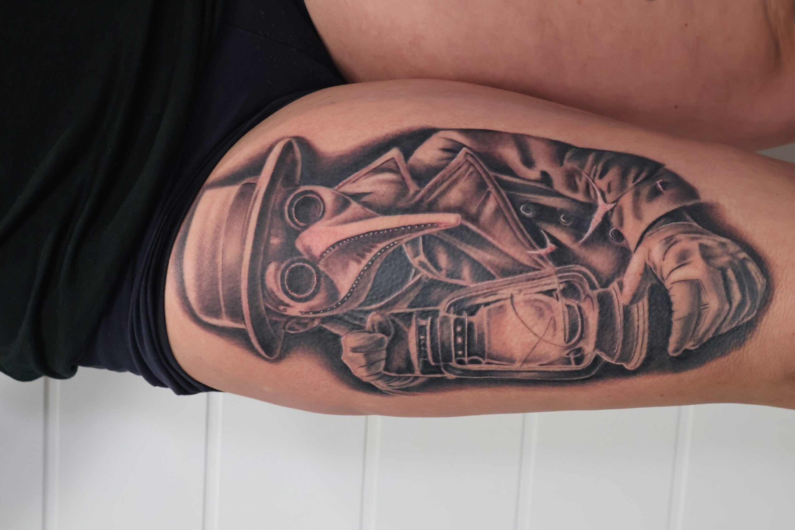 Tattoo of a helmet, sword, and shield on a person's upper arm, with detailed shading and realistic style.