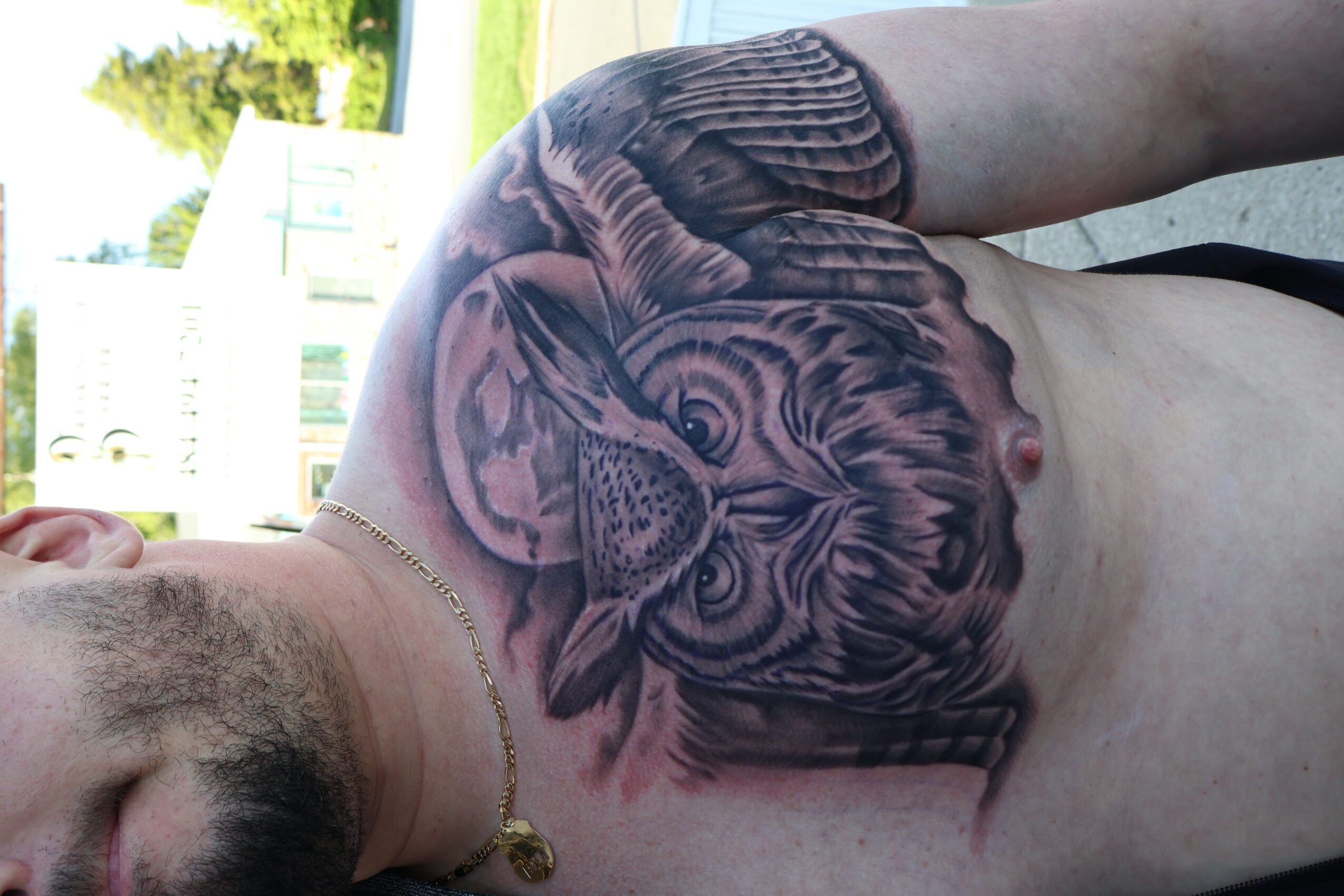 Person with a large tiger tattoo on chest, outdoors with trees and sky in background.