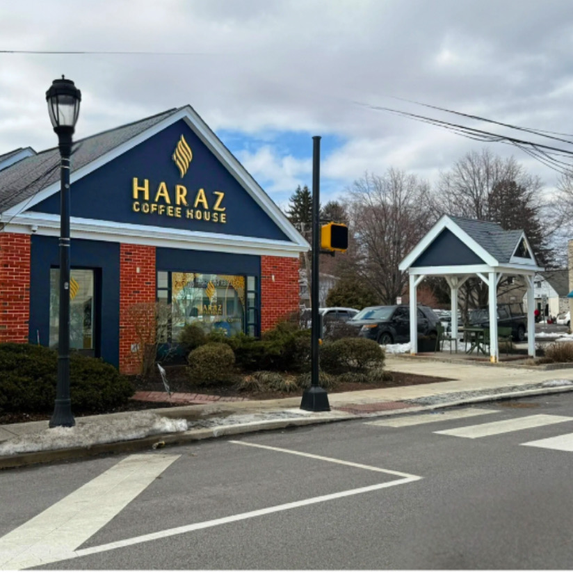 Haraz Coffee House building with a blue roof, brick walls, and a sign, next to a small white pavilion, on a cloudy day.