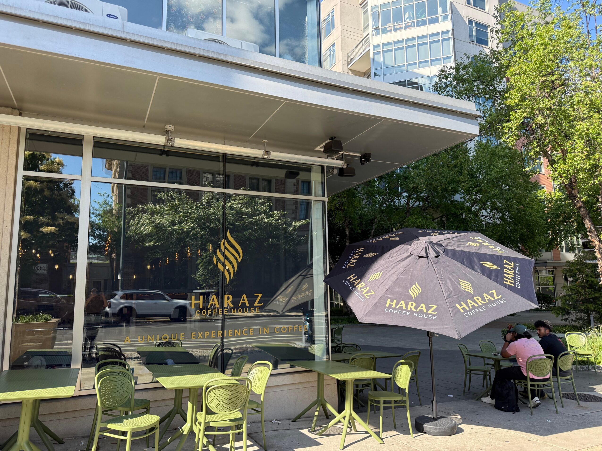 Outdoor seating area with green chairs and tables outside a glass building, umbrella with