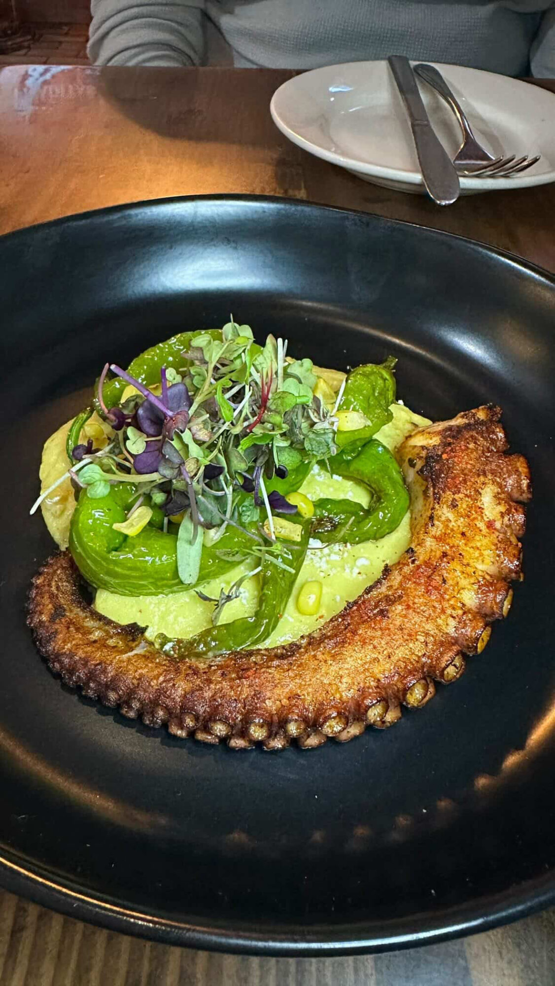 Fried fish fillet topped with sliced green vegetables and microgreens on a black plate.