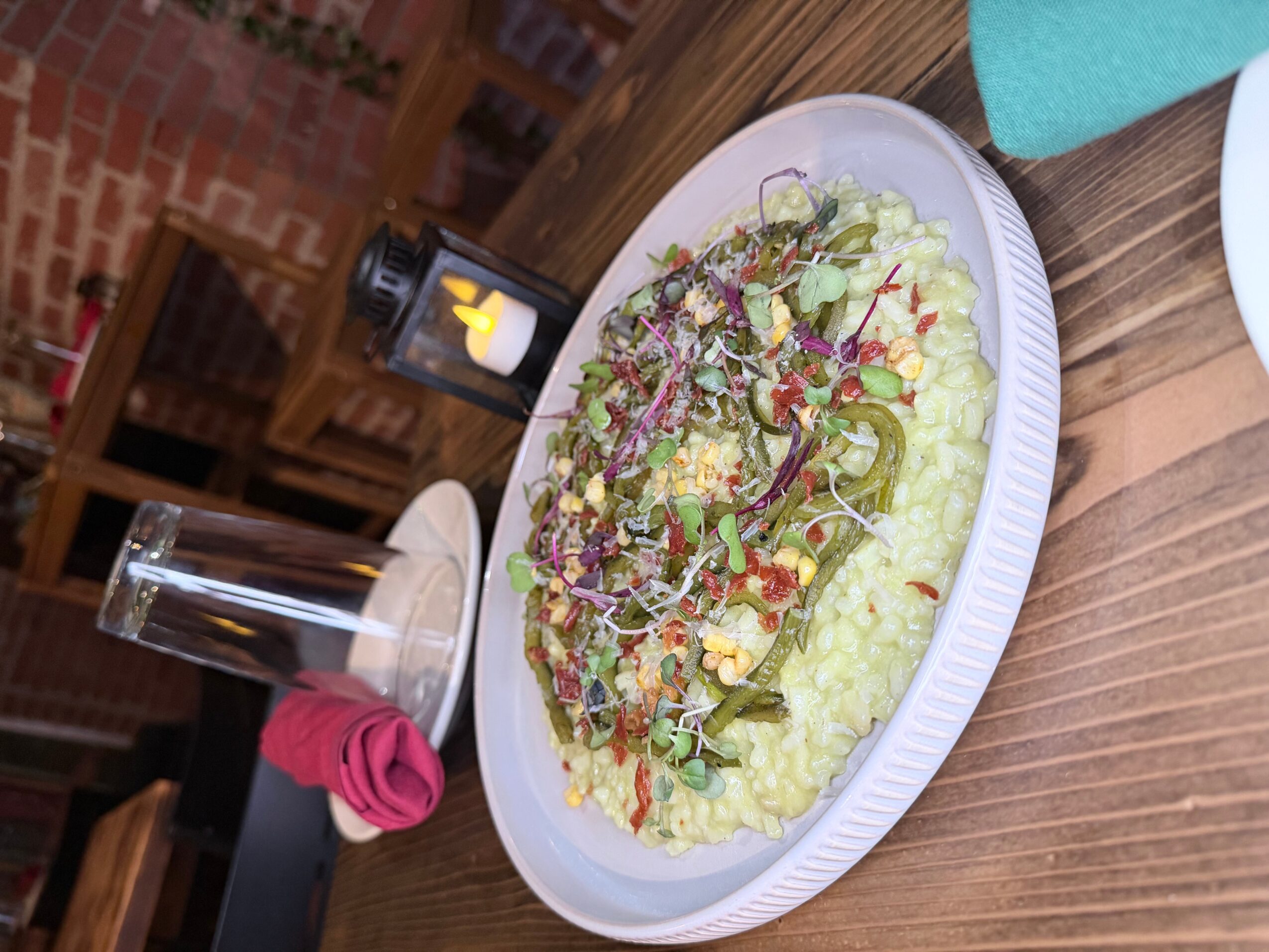 Plate of salad with lettuce, vegetables, and dressing on a wooden table, with a glass of water and a candle in the background.