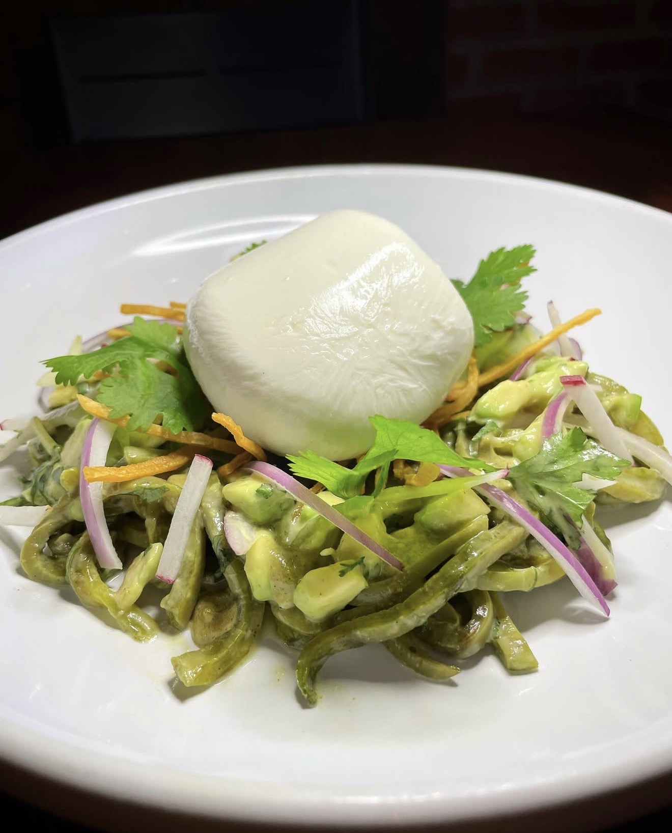Salad with green vegetables, red onion slices, and a dollop of white dressing or sauce on top, served on a white plate.