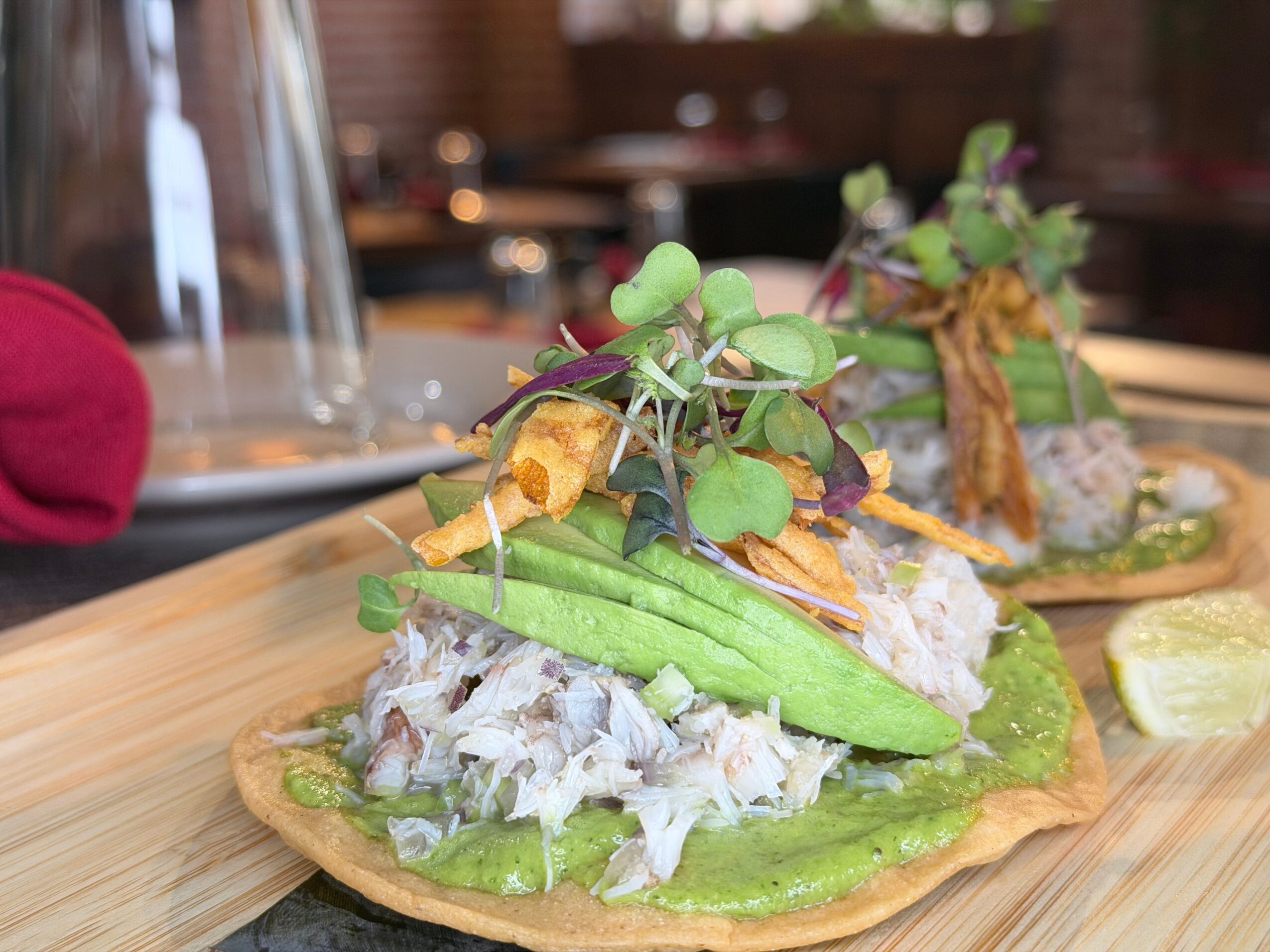 Open-faced sandwich with fish, cucumber, and greens on a wooden board, with lemon wedge and blurred background.