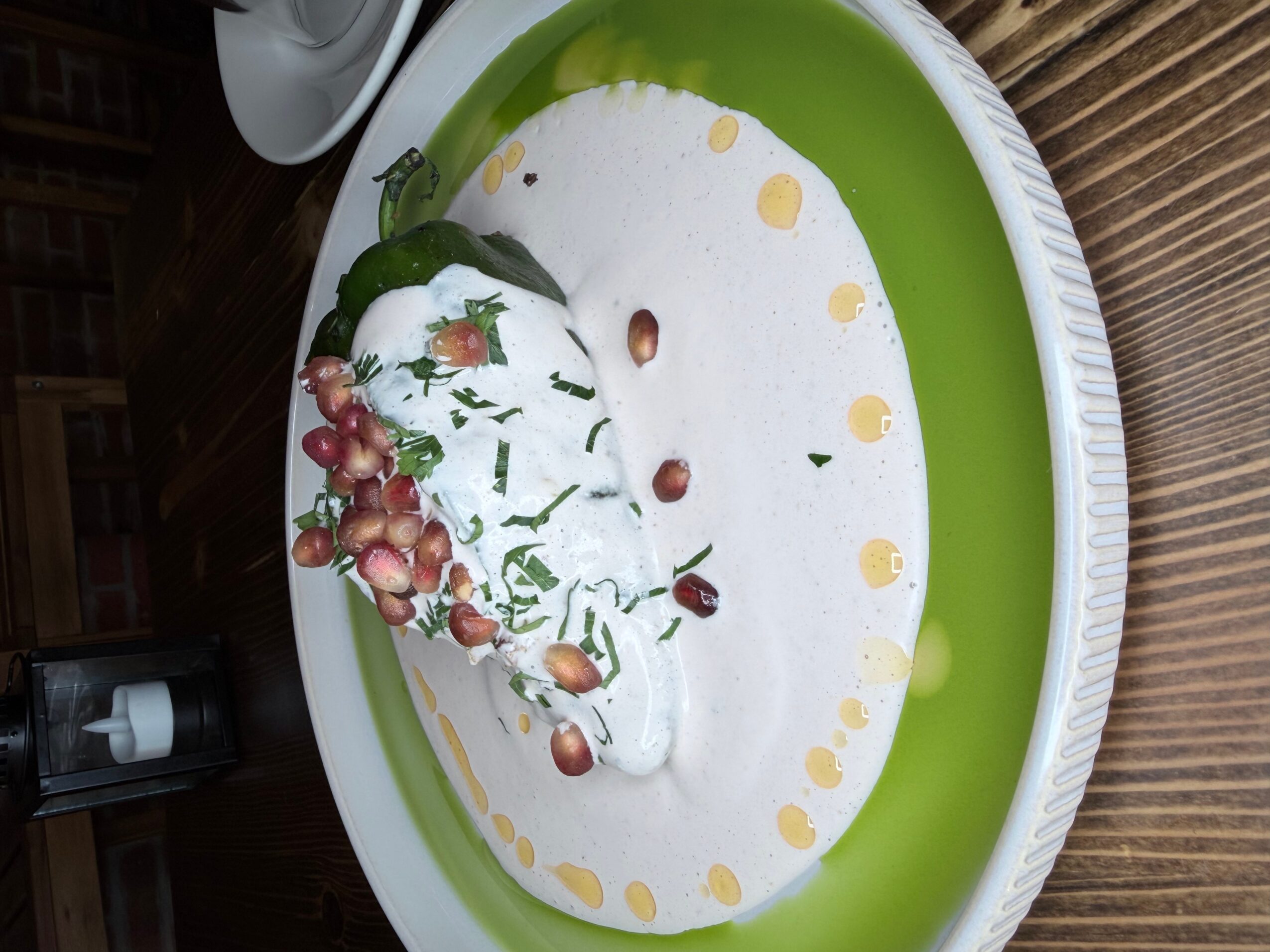 A bowl of creamy dessert topped with whipped cream, grapes, and nuts, on a green and white plate.