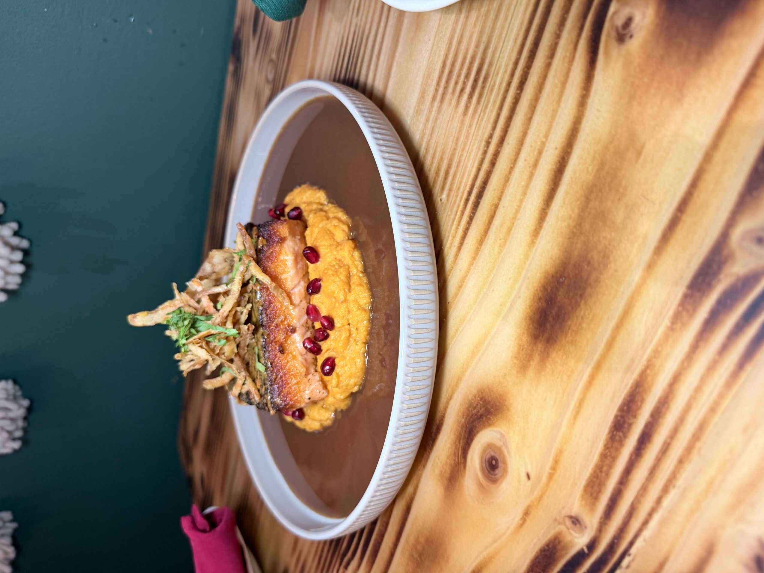 A plate with a decorated dish on a wooden table, with a green wall in the background.