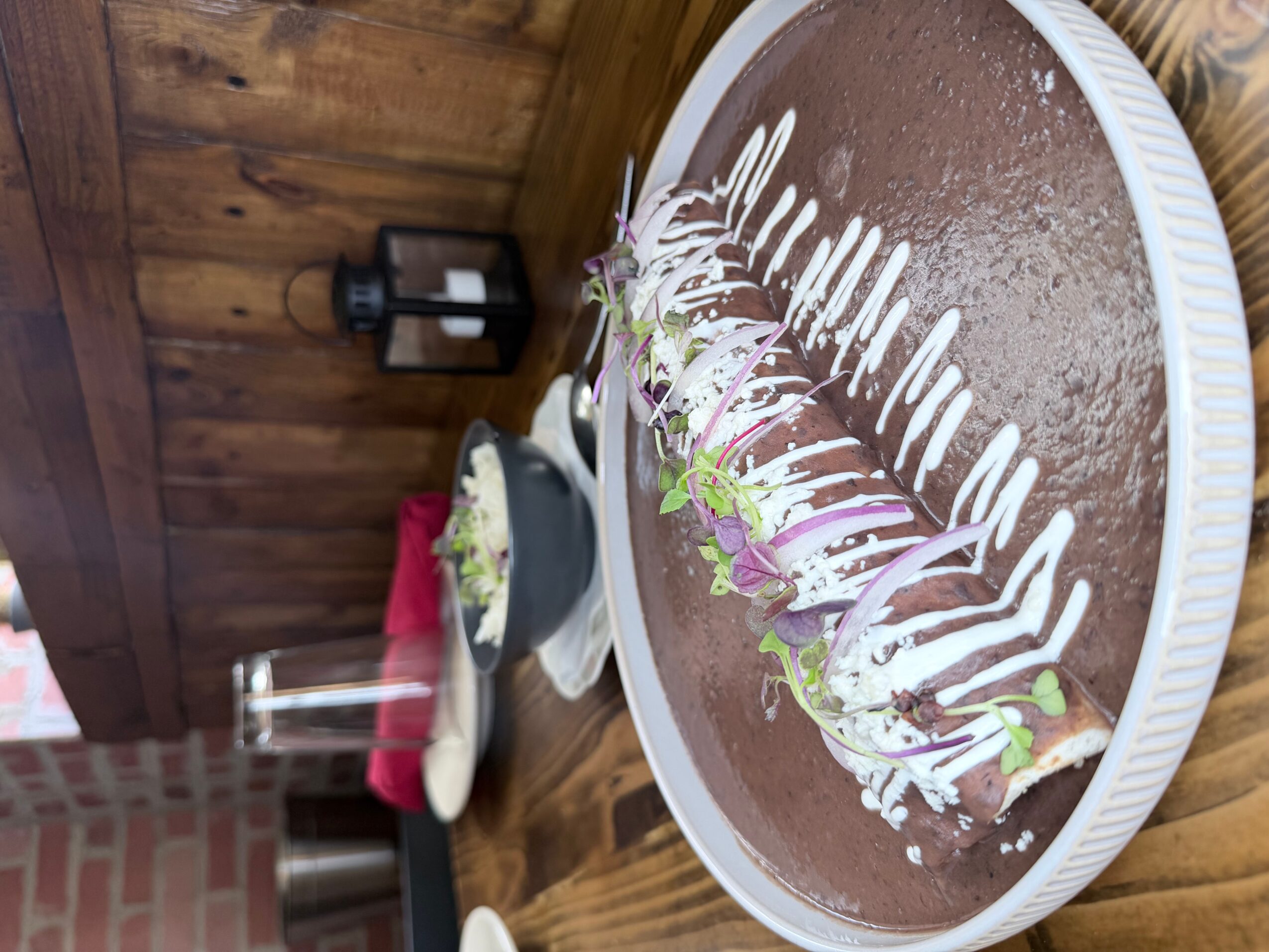Chocolate cake with white icing decoration and small flowers on top, on a round white tray, on a wooden table.