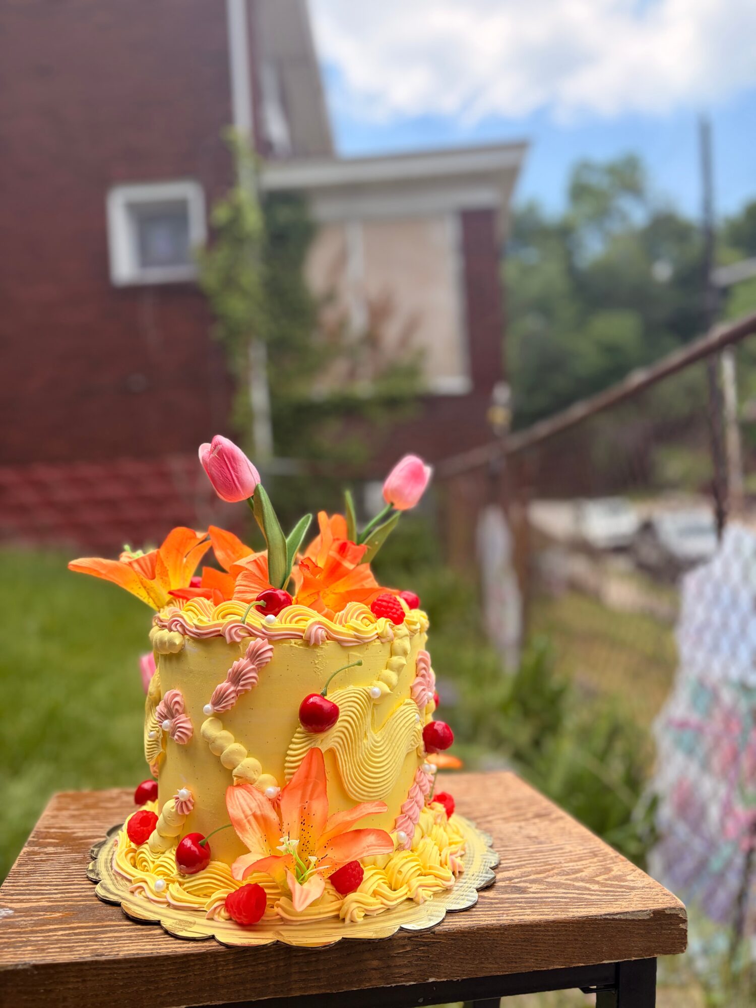Decorative cake with pink tulips and orange flowers, adorned with red berries, on a wooden surface outdoors.