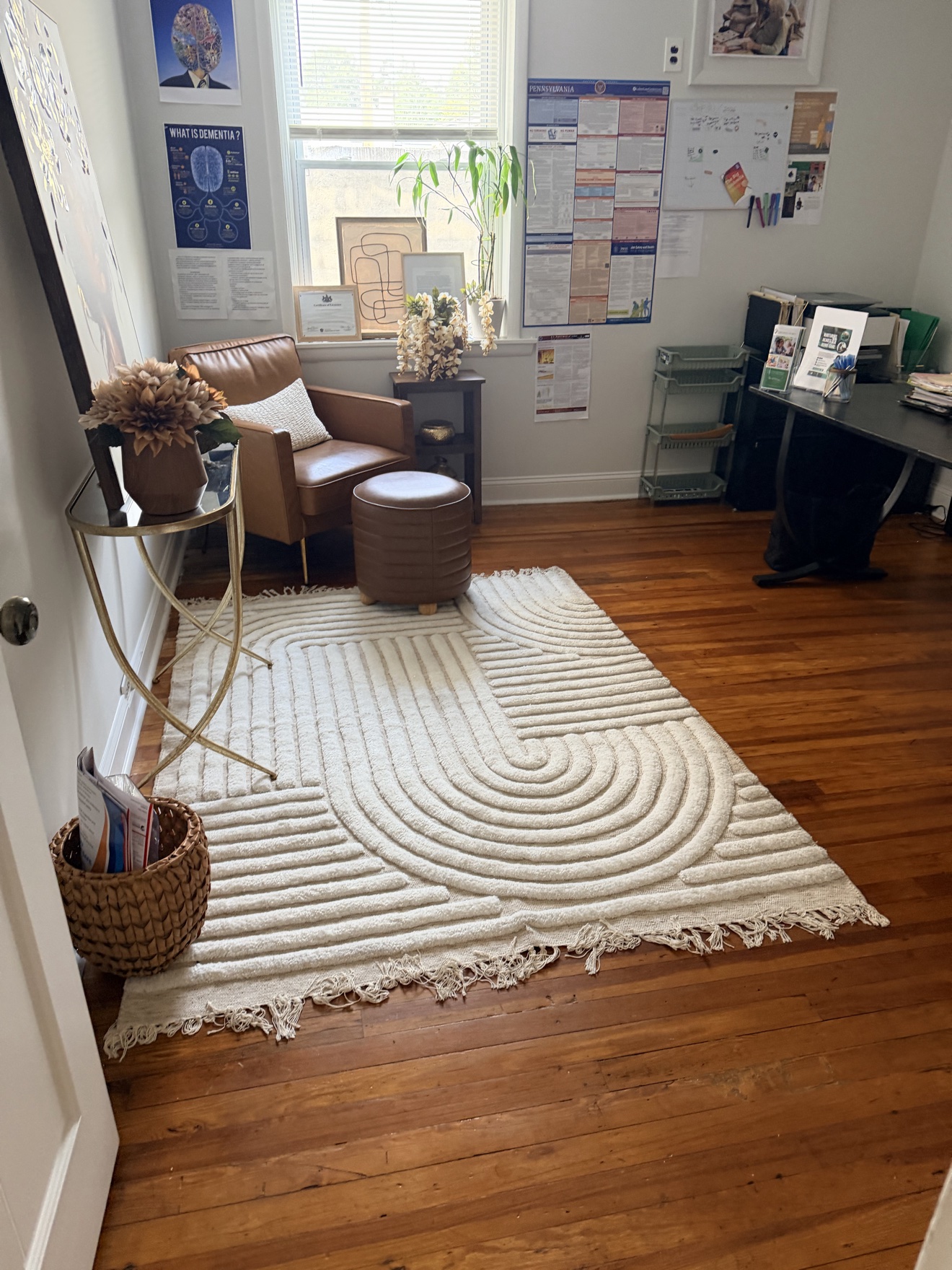 Room with a window, armchair, small table, and a white textured rug on wooden floor.